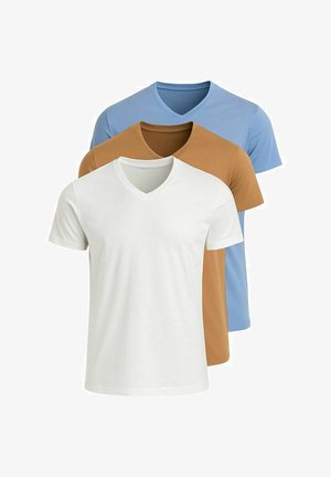 Tan V-hals t-shirt gecombineerd met witte, op maat gemaakte broek en donkere instap schoenen, die een getailleerd ontwerp en een soepele stofstructuur tonen.