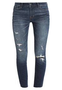 Mörkblå skinny jeans med en slitna design. Har revader på knäna och en lätt blekning, tillverkade av denim.
