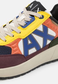 Sneaker multicolore con un mix di materiali: rete, pelle e gomma. Include un logo prominente, accenti testurizzati e suola beige.