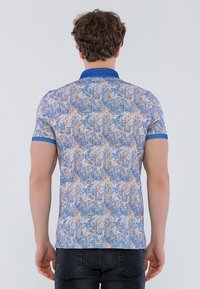 Polo de manga corta en un patrón texturizado azul y beige, con cuello azul y acentos en los puños. La tela parece ligera y casual.
