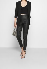 Czarna marynarka nałożona na krótki czarny top, zestawiona z błyszczącymi czarnymi spodniami z ekoskóry oraz czarnymi sandałkami na wysokim obcasie. Dopełnieniem jest mała metaliczna torebka.