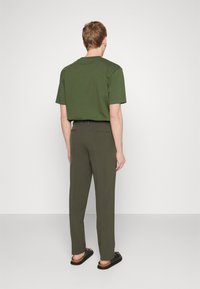 T-shirt de algodão verde, com corte descontraído, combinado com calças verde-azeitona. O modelo usa sandálias pretas. Design simples, sem padrões ou logótipos visíveis.