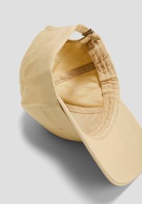 Gorra de béisbol color canela con visera curva, tejido suave y cierre con cremallera. El forro interior coincide con el color exterior, con costuras sutiles.