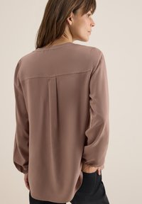 Hnědá blůza s dlouhým rukávem z lehkého materiálu, s uvolněným střihem, s prolisem na ramenou a nařasenými manžetami. Jednoduchý, minimalistický design.