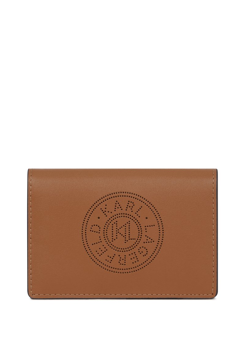 Hnědý kožený holder na karty s kulatým perforovaným logem umístěným na předním klopě, hladký povrch a viditelné prošívání podél okrajů.