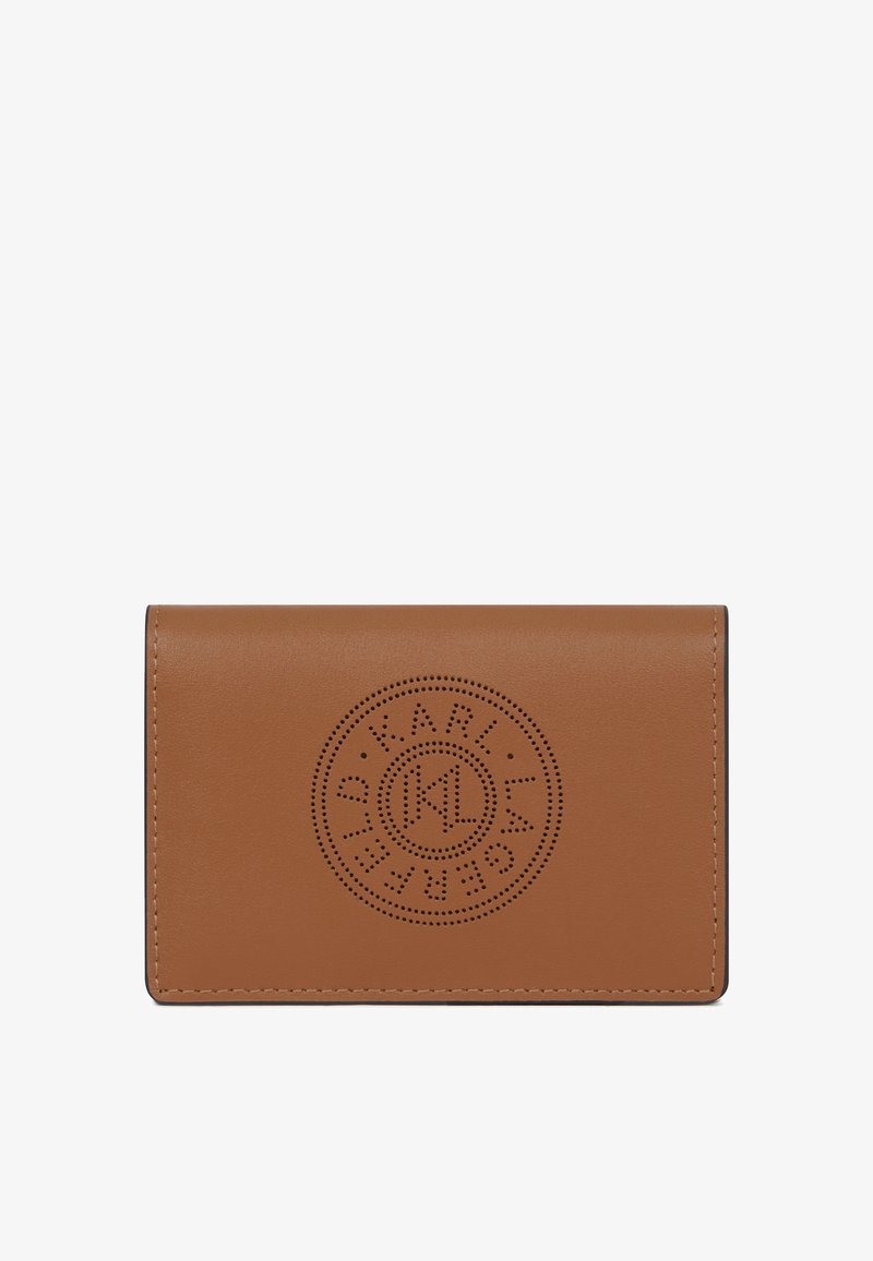 Hnědý kožený holder na karty s kulatým perforovaným logem umístěným na předním klopě, hladký povrch a viditelné prošívání podél okrajů.