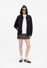 Crna zip-up dukserica s prednjim džepom, nosi se preko bijelog T-shirta. Uparen s blistavom suknjom i crnim tenisicama. Ležeran, opušteni kroj.