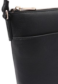 Zwarte leren tas met een gestructureerde afwerking, voorzien van een ritssluiting en een buitenzak. Accenten in vergulde hardware versterken het ontwerp.