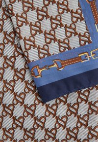 Foulard di seta con un motivo astratto marrone ripetitivo su uno sfondo chiaro, bordato con dettagli in blu e blu scuro.