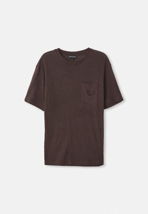 T-shirt marron à manches courtes en tissu doux et texturé, avec une petite poche sur le côté gauche et un col rond.