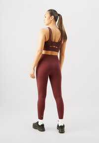 Burgunder sports-bh og høyt liv leggings i et glatt, elastisk stoff. Bjørnen har flerstriper, og leggings har en tettsittende silhuett.