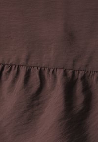 Tissu marron avec une couture froncée créant des plis doux et une variation de texture sur le tissu.