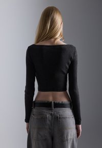 Black ribbed long-sleeve top with a wide neckline, paired with high-waisted grey denim jeans featuring back pockets and a black belt.