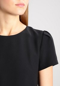 Robe noire à manches courtes bouffantes, en tissu lisse. Elle présente un col rond et une silhouette ajustée. Design épuré et minimaliste.