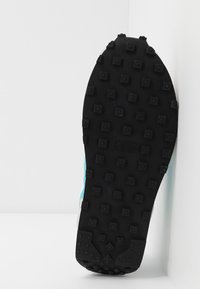 Černá gumová podrážka obuvi s čtvercovými výstupky, s modro-bílým bočním panelem. Design je ostrý a texturovaný pro lepší přilnavost.