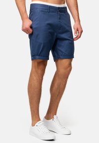 Shorts en coton bleu marine avec devant plat, revers roulés, poches latérales et ceinture classique ; assortis à des baskets blanches.