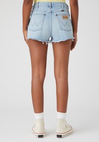 Světle modré džínové šortky s třepenými lemy, dvěma zadními kapsami s cikcak vzorem a tkanou etiketou na pravé kapse.