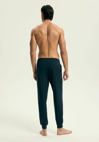 Granatowe spodnie dresowe wykonane z miękkiego materiału, z elastycznym pasem i zwężającymi się nogawkami zakończonymi ściągaczami. Brak widocznych wzorów lub metalowych elementów.