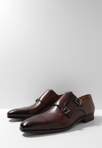 Chaussures en cuir marron avec une finition polie, dotées de sangles à double boucle, d’un bout pointu et de détails de coutures subtils.