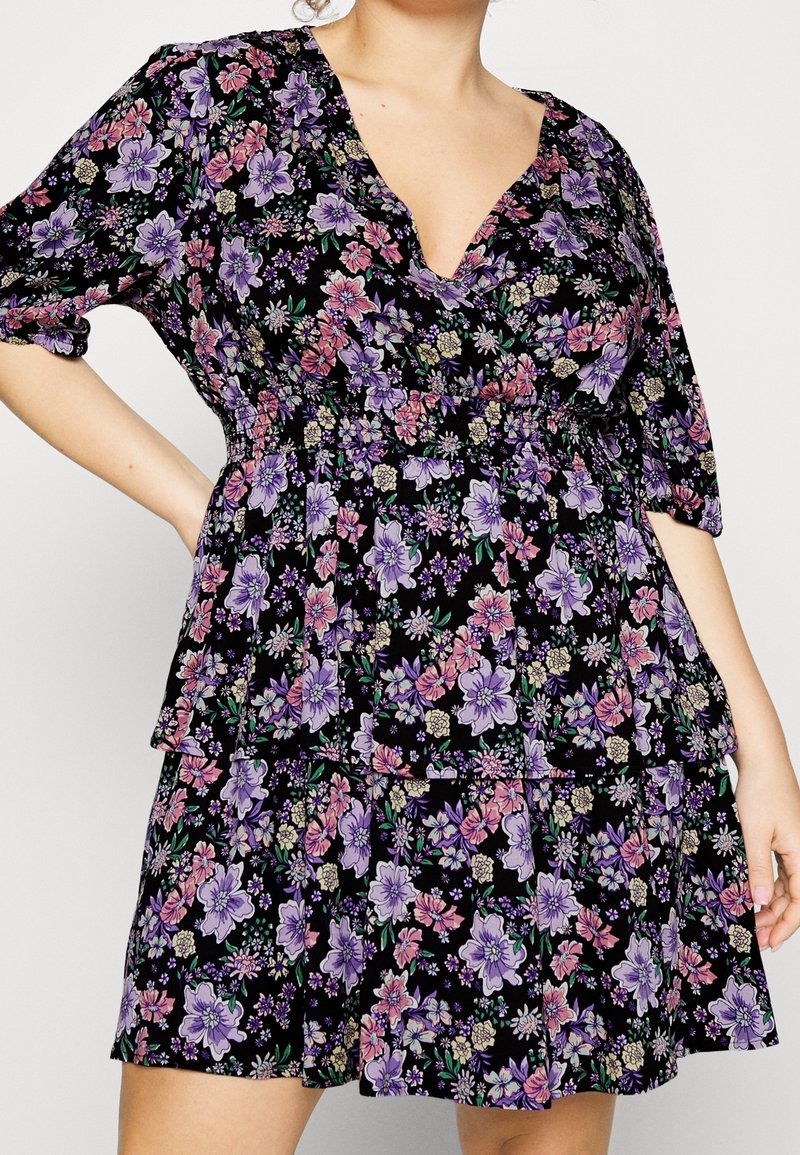 Robe noire à fleurs avec un décolleté en V, des manches courtes bouffantes et un ourlet en volants à étages. Présente des fleurs violettes et roses sur un fond sombre.