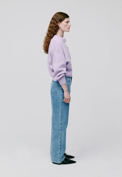 Übergroßer Lavendelpullover mit Rundhalsausschnitt, kombiniert mit hellblauen, hoch taillierten Jeans und spitzen schwarzen Ankle-Boots. Glatte Textur.