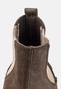 Botín de ante marrón con textura suave, paneles laterales elásticos y un collar acolchado con detalles de costura en las costuras.
