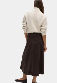 Maglione beige a coste con collo alto, abbinato a una gonna midi in suede marrone scuro. L'outfit presenta una vestibilità rilassata e nessun motivo visibile.