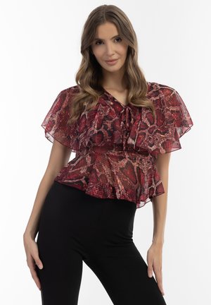 Rød og sort slangeskindsprint peplum top med gennemsigtige flæseærmer og en sløjfe ved halsen, båret med tætsiddende sorte bukser.