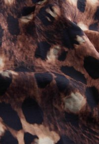 Tissu marron à texture douce présentant un motif léopard avec des taches noires et beiges, montré avec des plis et des ombres naturelles.