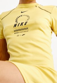 Gele Nike t-shirt met korte mouwen, voorzien van zwart gedrukt logo en tekst. Glad textuur met contrasterende stikdetails.