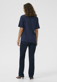 Marineblaues T-Shirt mit kurzen Ärmeln und Rundhalsausschnitt, kombiniert mit dunklen Jeans. Glatte Stofftextur, lockere Passform und keine sichtbaren Muster.