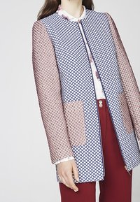 Lightweight jacket with a geometric blue and white patterned front and sheer, textured pink long sleeves. Features front pockets and a zip closure.