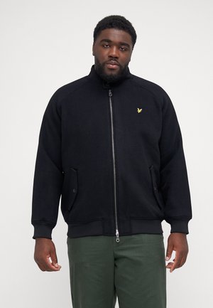 Black zip-up sweatshirt with a stand collar, featuring a small yellow logo, raglan sleeves, and front pockets. Smooth texture and relaxed fit.