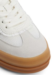 Sneaker bianca e grigia chiara con tomaia in suede, dettagli in rete e suola in gomma naturale. Texture liscia con lacci piatti e cuciture sottili.