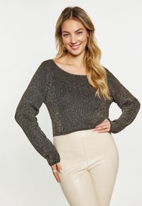 Pullover tricotat metallic negru și auriu, cu mâneci lungi și un decolteu larg, asortat cu pantaloni bej conici. Textură netedă și design scurt.
