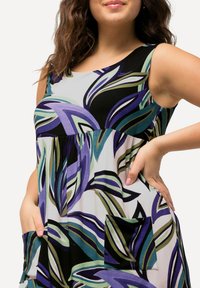 Vestido sin mangas con estampado floral que presenta tonos de púrpura, verde y negro. Incluye bolsillos laterales y una silueta suelta y fluida.