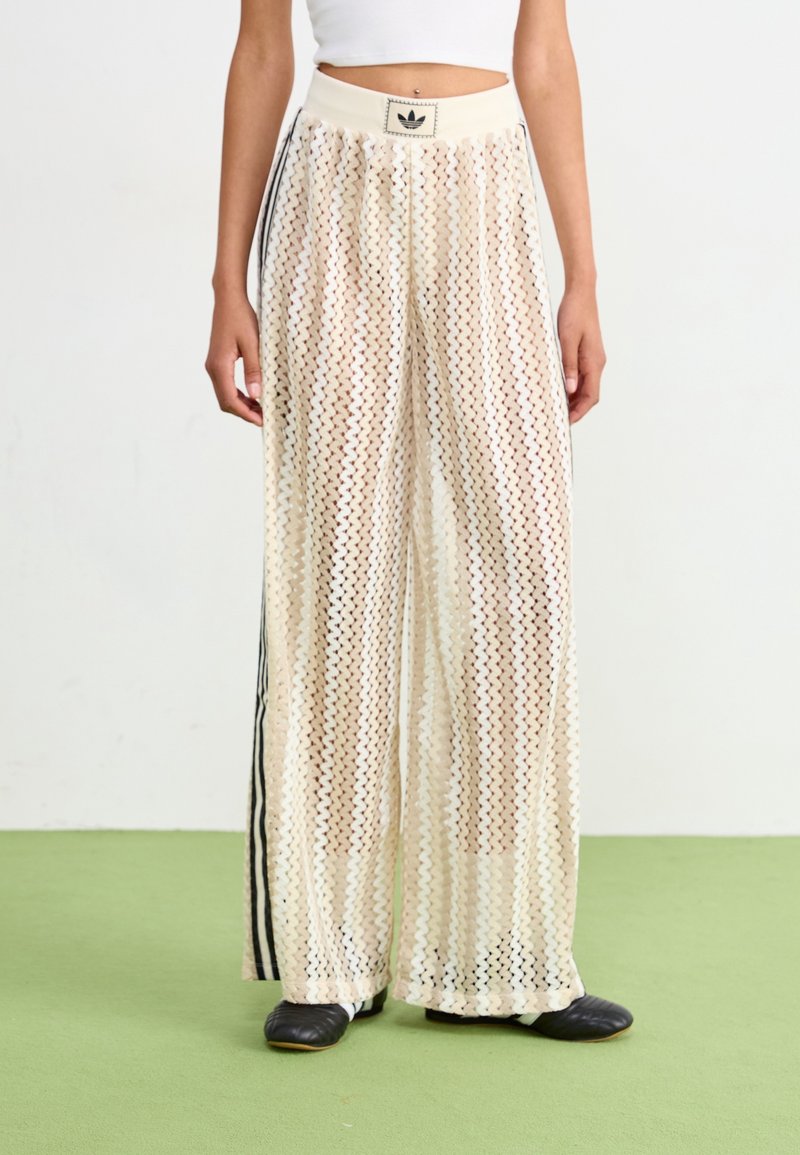 Kreeminväriset laiad püksid, mis on valmistatud transparentsest, tekstuuriga kangast, millel on vöötkrae muster, kontrasteeriva musta külgtriibuga ja elastse vööga.