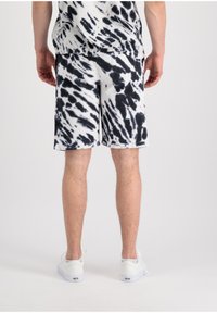 Kratke hlače tie-dye u bijeloj i crnoj boji, napravljene od mekanog materijala, s bočnim džepovima i opuštenim krojem, uparene s bijelim tenisicama.
