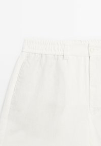 Pantalons en lin blanc avec une taille à cordon, dotés d'une fermeture à bouton et de poches latérales, mettant en valeur un tissu lisse et texturé.