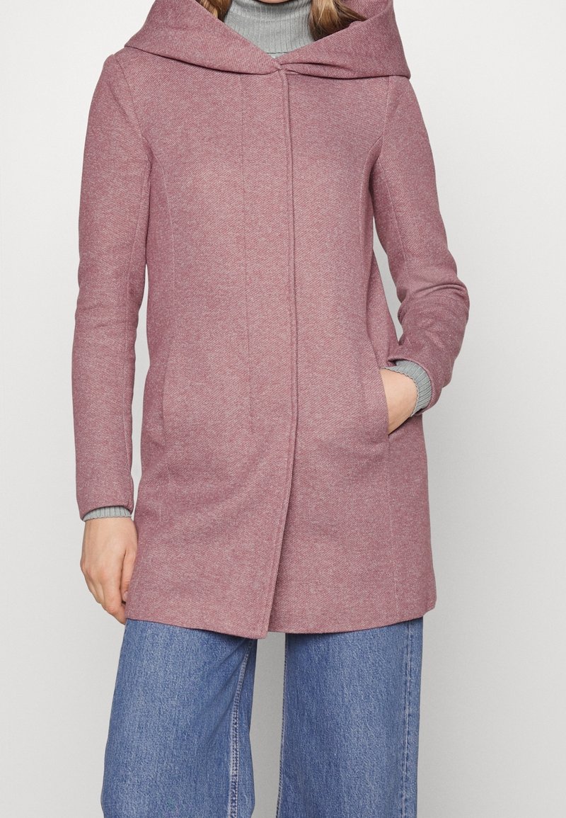 Long, textured coat in a soft rose hue with a wide, draped hood and side pockets. Features a straight cut and ribbed cuffs.