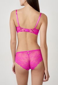 Ensemble en dentelle fuchsia comprenant un soutien-gorge avec fermeture à l'arrière, orné de broderies florales, et un bas transparent assorti avec un détail en nœud.
