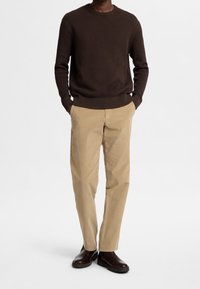 Jersey de punto marrón texturizado, pantalones de pana beige y botines oscuros marrones. El jersey tiene cuello redondo y dobladillo acanalado.