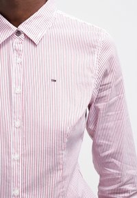 Rood-wit gestreepte blouse met lange mouwen en een button-down kraag, voorzien van een klein logo op de borst en een knoopsluiting.