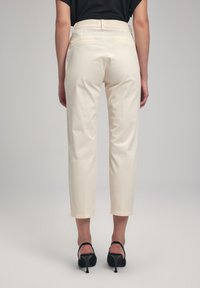 Cream-colored trousers with a tapered leg design. Features a smooth texture, two back pockets, and a mid-rise waist. Worn with black heels.