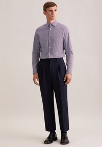 Overhemd met knoopsluiting in marineblauw en wit geometrisch patroon, gecombineerd met op maat gemaakte donkere broeken. Zwarte leren schoenen maken de outfit compleet.