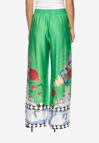 Zelené saténové kalhoty palazzo s květinovými a dekorativními potisky, širokými nohavicemi, elastickým pasem a kontrastním černo-bílým vzorovaným lemem.
