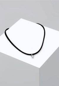 Schwarzes Schnur-Halsband mit einem silbernen Pendant in Form einer Kugel, das eine glatte Textur und ein einfaches Design aufweist, auf einem weißen geometrischen Display ruht.
