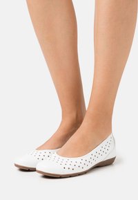 Vita ballerinaskor med perforerat ovandel, rund tå och flexibel brun sula. Lätta syntetiska material med slät yta.