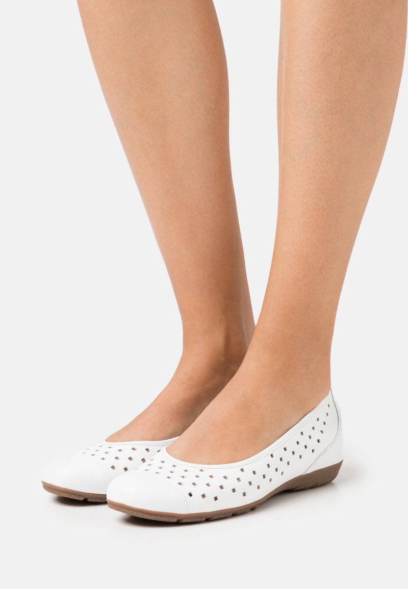 Vita ballerinaskor med perforerat ovandel, rund tå och flexibel brun sula. Lätta syntetiska material med slät yta.