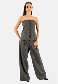 Top grigio senza spalline con bottoni sulla parte anteriore, abbinato a pantaloni grigi a gamba larga. Entrambi i capi hanno una finitura texture.